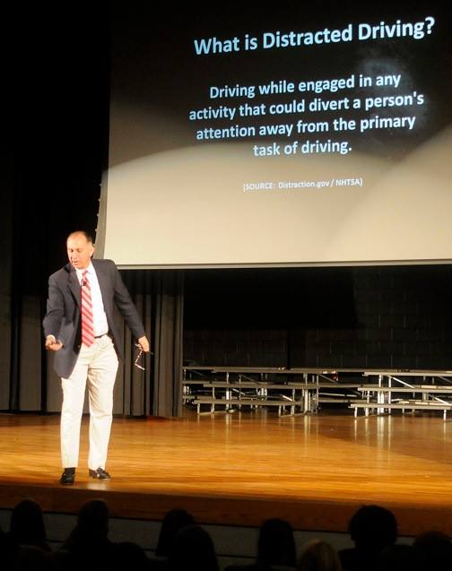 George Jebaily acting out the distraction of texting on a phone on stage at a distracted driving event