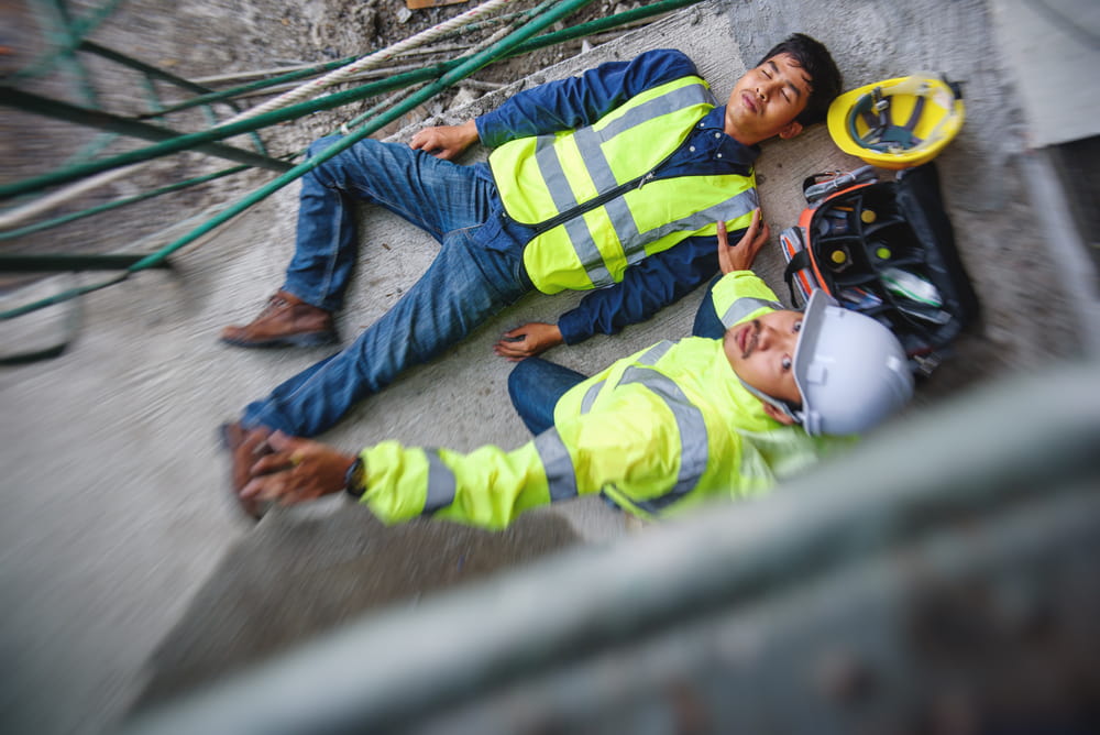 bird's eye view of construction worker lying injured on the pavement while another worker looks up at the scaffold in the foreground