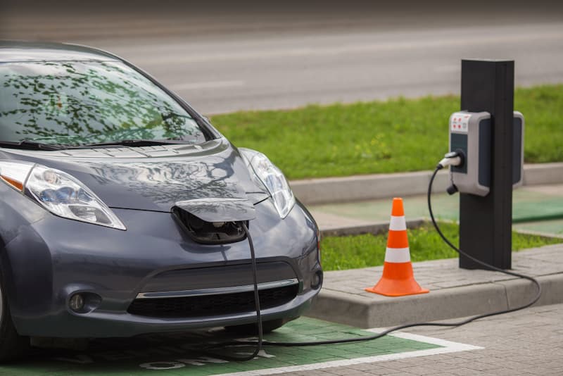 An electric car plugged into a charging station with a traffic cone placed nearby.