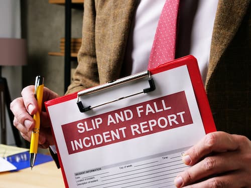 A person holding a clipboard with a "Slip and Fall Incident Report" form.